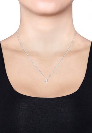 Silberne Halskette mit einer zarten Kette und einem kleinen Buchstaben "J"-Anhänger, getragen auf einem nackten Hals über einem schwarzen Oberteil.