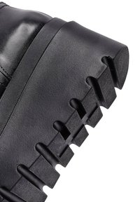 Czarne skórzane botki na platformie z masywną podeszwą, charakteryzujące się głębokimi rowkami i gładką powierzchnią, podkreślające solidny design.