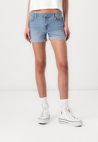 Ljusblå denimshorts med uppvikta fållar, femfickorsdesign och knäppning med knapp. Bärs tillsammans med vita högklackade sneakers och längdstrumpor.