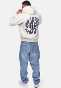 White hoodie with a large, dark graphic text on the back saying "DROPSIDE GREEN LOVE." Paired with loose light blue jeans and white sneakers.