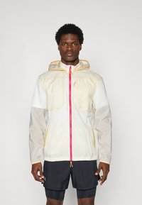 Giacca leggera con cappuccio in beige e bianco, con zip rosa e dettagli gialli; presenta due tasche frontali e orlo elastico.