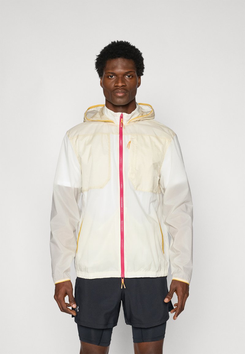 Giacca leggera con cappuccio in beige e bianco, con zip rosa e dettagli gialli; presenta due tasche frontali e orlo elastico.