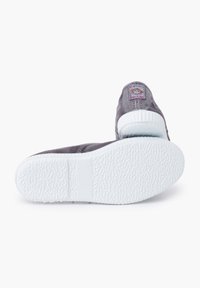 Zapatillas de tela grises con una suela texturizada blanca, que presentan una etiqueta colorida en el talón y costuras en contraste.