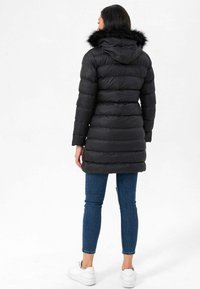 Sort pufferjakke med hætte og faux fur-kant, udstyret med horisontale quilte-puder. Kombineret med blå tætsiddende jeans og hvide sneakers.