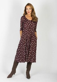 Brązowa sukienka w kropki o fasonie A, z rękawami 3/4, kieszeniami oraz miękkim, elastycznym materiałem, zestawiona z brązowymi botkami do kolan.