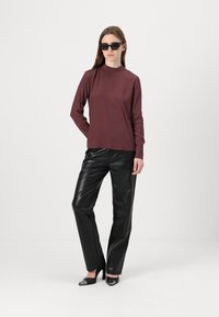 Maroon long-sleeve top with high neckline paired with black faux leather trousers, featuring a smooth texture and shiny finish. Black sunglasses.