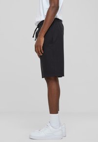 Pantalones cortos de algodón negros con cintura elástica y cordón. Bolsillos laterales y un ajuste holgado, combinados con zapatillas blancas y calcetines cortos.