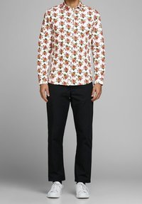 Biała koszula na guziki z kwiatowym nadrukiem przedstawiającym czerwone i zielone róże, w zestawieniu z czarnymi spodniami i białymi tenisówkami.