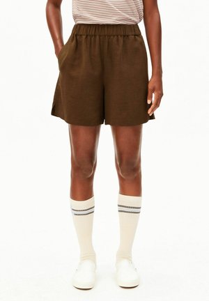 Personne portant un short marron à taille élastique, un t-shirt rayé, des chaussettes blanches montantes avec des rayures grises, et des chaussures blanches sans lacets.