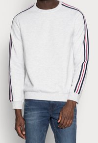 Sudadera gris con franjas blancas, rojas y azul marino a lo largo de las mangas, con cuello redondo y puños acanalados, hecha de un material de felpa suave.