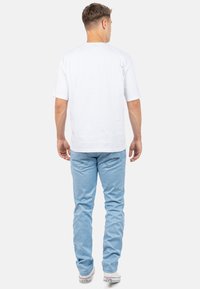 Witte T-shirt met korte mouwen gecombineerd met lichtblauwe spijkerbroek. T-shirt heeft een ronde hals; de spijkerbroek heeft een textuurpatroon en standaardzakken.