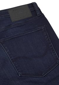Jeans in denim blu scuro con una tasca posteriore con cuciture curve e un'etichetta in pelle nera in vita. Texture liscia, vestibilità slim.