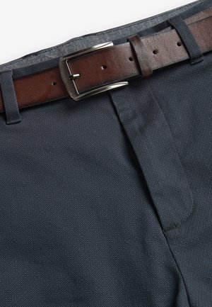 Brunt læderbælte med sølvspænde fastgjort på linningen af marineblå teksturerede bukser.