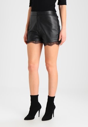 Vrouw draagt zwarte leren shorts met kanten rand, gecombineerd met zwarte soklaarzen met hoge hak.