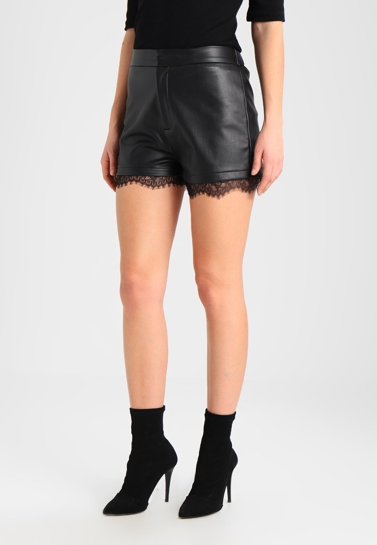Femme portant un short en cuir noir avec bordure en dentelle, associé à des bottines chaussettes noires à talons hauts.