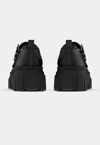 Baskets plateformes noires avec une semelle en caoutchouc texturée, dotées d'une tige en cuir lisse et d'accents de boucles ajustables.