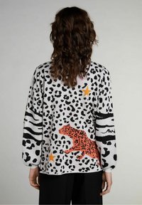 Gebreide trui met een luipaardprint in zwart en wit, met een oranje luipaardontwerp en zwarte horizontale strepen. Lange mouwen en een ontspannen pasvorm.