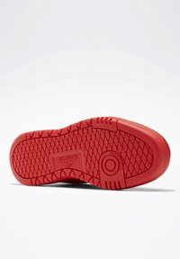 Czerwony spód buta Reebok z wzorem o diamentowym bieżniku, okrągłym obszarem chwytowym oraz napisem "niepozostawiająca śladów podeszwa" na gładkim białym tle.