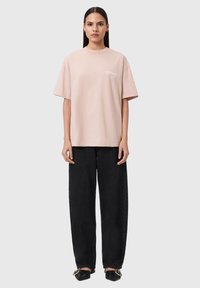 Oversized roze katoenen T-shirt met een ronde hals en korte mouwen, gecombineerd met zwarte high-waisted spijkerbroek en zwarte schoenen.