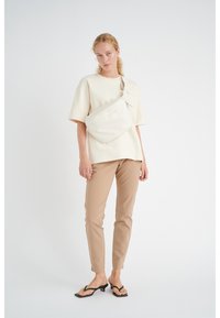 Creme kortærmet top med en brystlomme, beigemelange fitted bukser og sorte sandaler med remme. Glat tekstur; minimalistisk design.