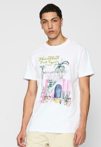 Hvid kortærmet t-shirt med et farverigt akvarelmotiv af en dør med planter, teksten "Marrakech Fruits Export" og en citron.