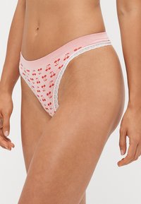 Ružičasti pamučni bikini s printom trešanja, rebrastom teksturom i čipkastim rubom na struku. Dizajn sadrži male crvene trešnje raspoređene po cijelom biku.