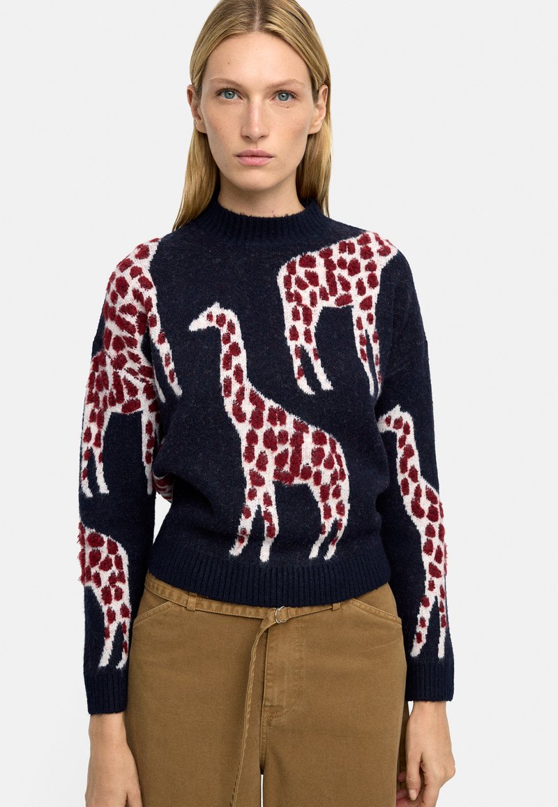 Granatowy sweter z teksturowanym wzorem żyrafy w czerwono-białe pasy. Ściągaczowy dekolt i rękawy, miękka tkanina o luźnym kroju.
