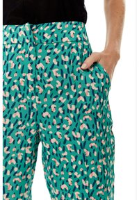 Teal pants with a textured fabric, featuring a colorful abstract pattern in pink and navy. Includes side pockets and a flat waistband.