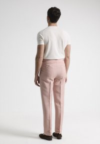 Pantalones rosa claro con un corte a medida, bolsillos traseros y una textura sutil. Combinados con una camisa blanca de manga corta ajustada.