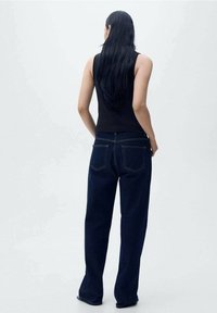 Ciemnoniebieskie dżinsy o szerokim kroju, z dwoma tylnymi kieszeniami i kontrastowym żółtym przeszyciem. Noszone z czarnym topem na ramiączkach.