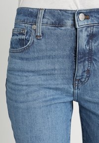 Light blue denim jeans with a faded wash, five-pocket design, metal button and zipper hardware, and contrasting stitching detail.
