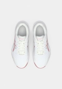 Le scarpe da ginnastica bianche presentano materiali in pelle liscia e tessuto a rete, con accenti rosa e una suola multitexturizzata. I lacci e il logo sono visibili sulla linguetta.