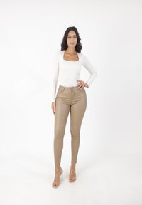 Top blanco de manga larga ajustado con escote cuadrado, combinado con pantalones de cuero sintético color tan de cintura alta y sandalias de tacón bloque transparente.