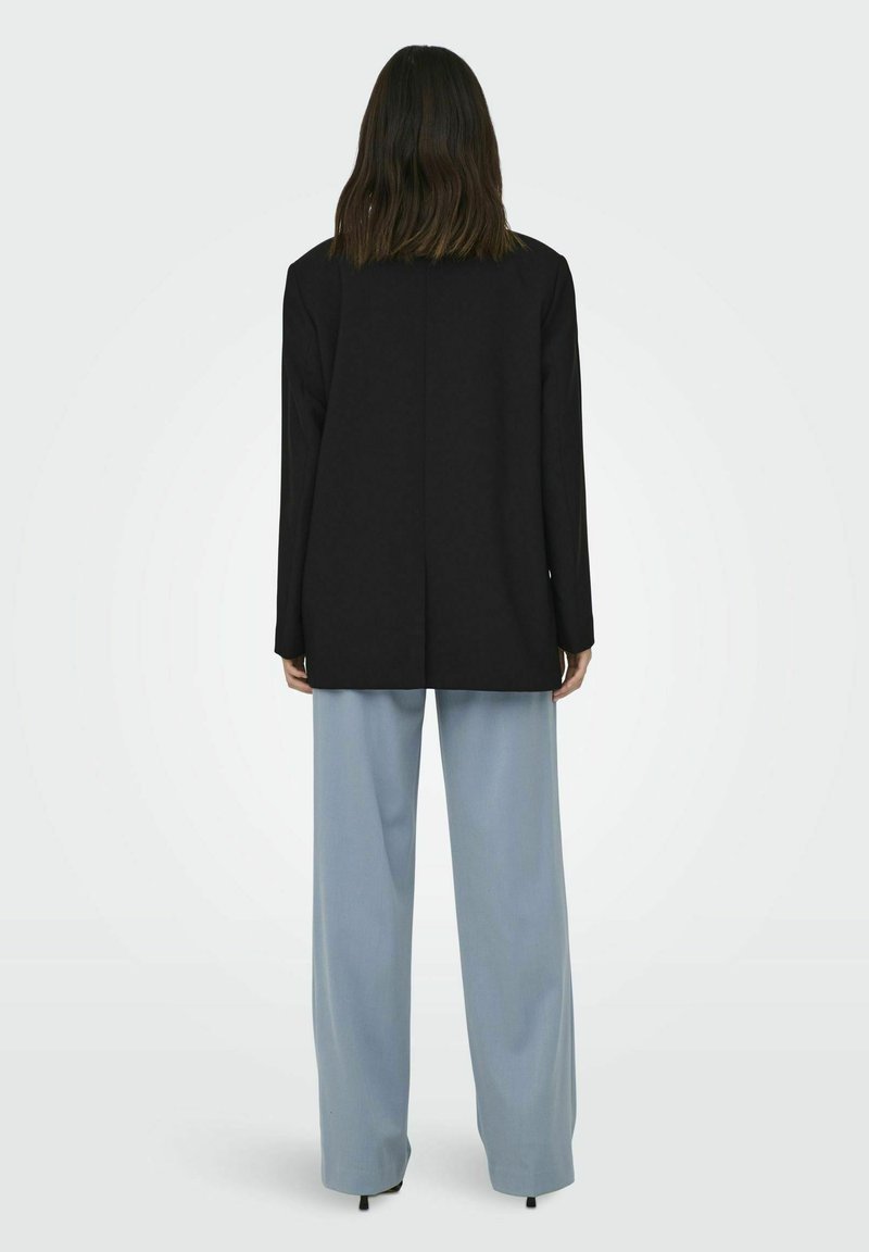 Schwarze Blazer mit langen Ärmeln und geradem Schnitt, kombiniert mit hellblauen, weit geschnittenen Hosen, die eine glatte Stofftextur und ein minimalistisches Design aufweisen.