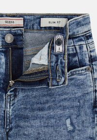 Dopasowane dżinsy w gradientzie od jasnoniebieskiego do ciemnoniebieskiego, z zamkiem błyskawicznym, naszywką z logo oraz przetarciami na tkaninie.