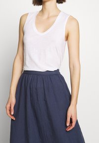 White sleeveless V-neck top paired with a dark blue high-waisted skirt, showcasing light, textured fabric and a relaxed fit.
