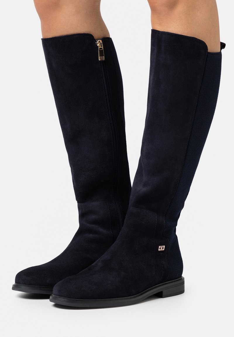 Knähöga marinblå mockastövlar med sidodragkedja, texturerad tyg, rund tå och platt gummisula med en liten metallaccent.