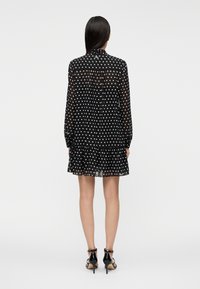 Μαύρο φόρεμα με πουά, μακριά μανίκια, βολάν στο τελείωμα και διαφανές ύφασμα. Διαθέτει γιακά με κουμπιά και κανονική εφαρμογή. Φορεμένο με μαύρα τακούνια.