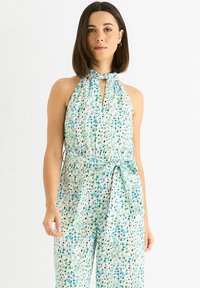 Floral jumpsuit in light fabric with a halter neck, features a keyhole opening, tie waist, and a pattern of blue and green spots.