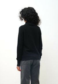 Zwarte gebreide trui met een hoge kraag, lange mouwen en geribde manchetten, gecombineerd met grijze tapered jeans. Zachte textuur, geen zichtbare patronen.