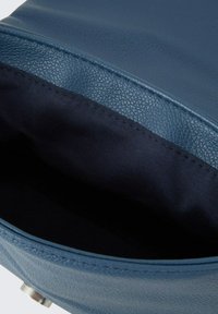 Borsa in pelle blu con un esterno testurizzato, che mostra un rivestimento in tessuto scuro all'interno. Presenta un'apertura liscia e arrotondata e cuciture visibili.
