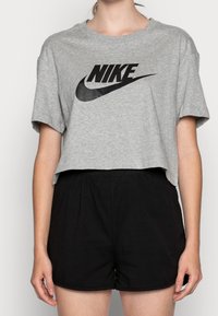 Grå kortärmad t-shirt med svart Nike-logotyp, rund hals. T-shirtsen är kombinerad med svarta shorts som har elastisk midja och slät textur.