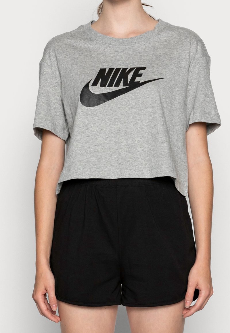 Grå kortärmad t-shirt med svart Nike-logotyp, rund hals. T-shirtsen är kombinerad med svarta shorts som har elastisk midja och slät textur.
