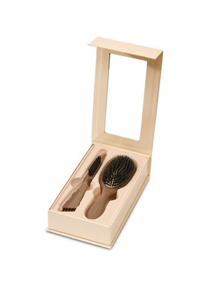 Kaksi beigeä hiusharjaa vastaavassa laatikossa, jossa muotoillut lokero ja avoin kansi, jossa suorakaiteen muotoinen peili.