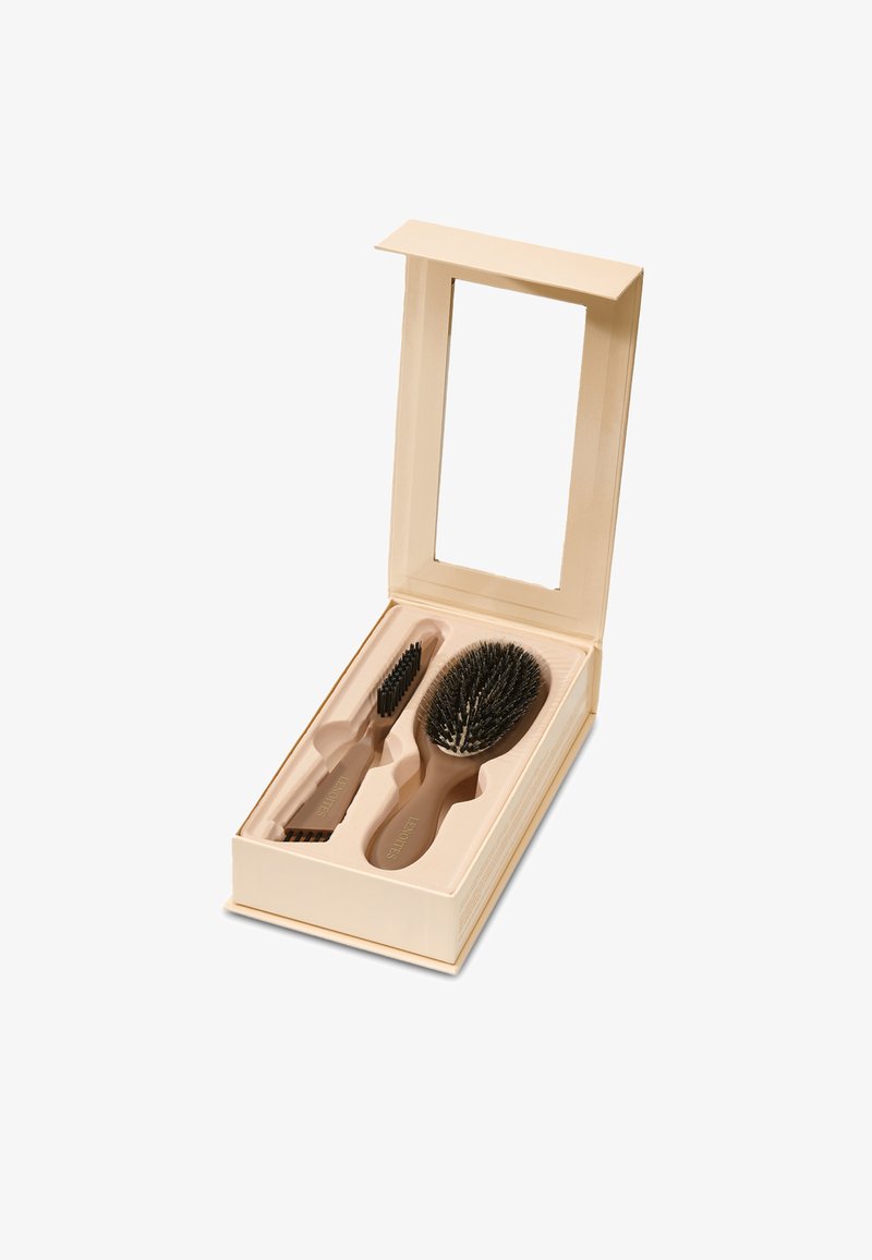 Deux brosses à cheveux beiges dans une boîte assortie avec compartiments moulés et un couvercle ouvert comportant un miroir rectangulaire.