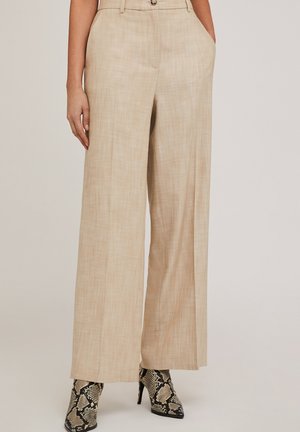 Pantalon large beige en tissu texturé, avec poches latérales et fermeture à bouton, associé à des escarpins à motif serpent noir et blanc.