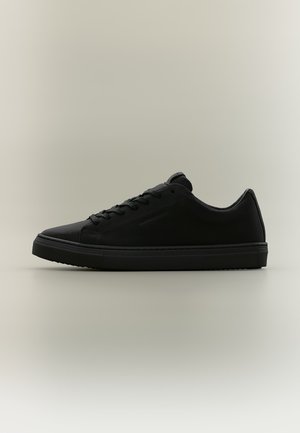 Μαύρο χαμηλό sneaker με κορδόνια μπροστά και υφή σόλας, απεικονίζεται σε ουδέτερο φόντο σε πλάγια όψη.