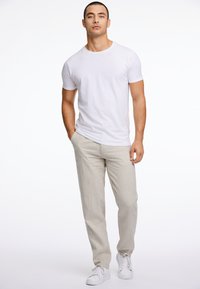 Wit T-shirt met korte mouwen, gecombineerd met lichtgrijze linnen broek. Model draagt witte sneakers. Glad textuur, casual pasvorm en neutrale kleuren.