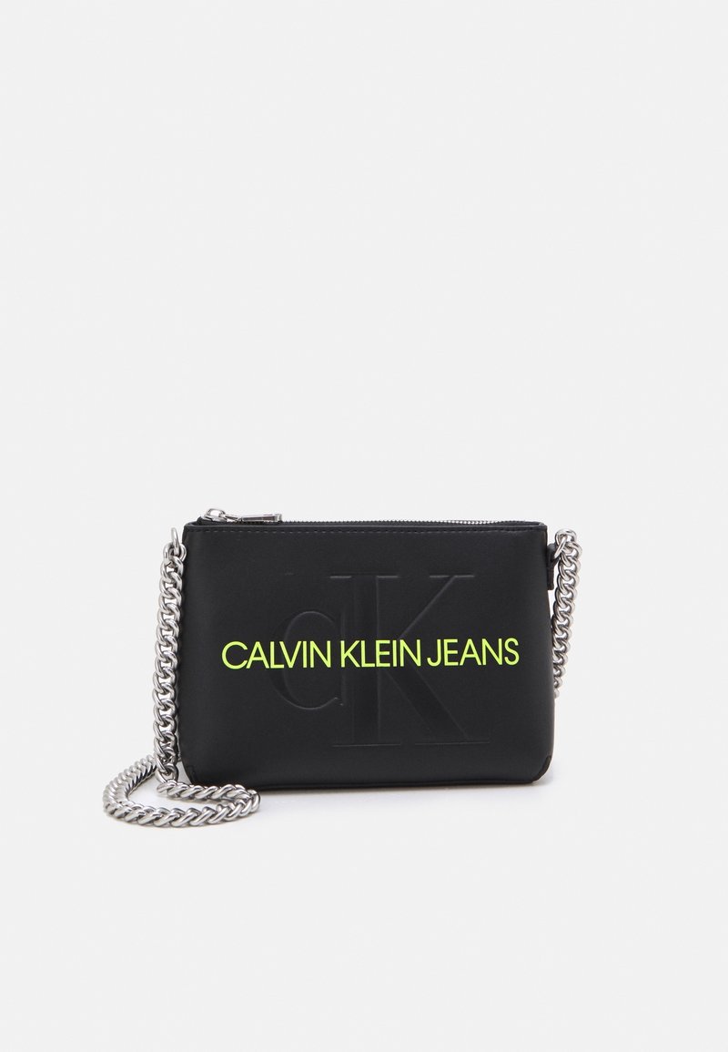 Borsa a tracolla nera in materiale sintetico con logo in rilievo e scritta gialla brillante "CALVIN KLEIN JEANS". Dotata di tracolla a catena argentata.