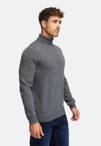 Pull en col roulé gris en tricot doux, design ajusté, poignets et ourlet côtelés. Porté avec un jean en denim bleu.